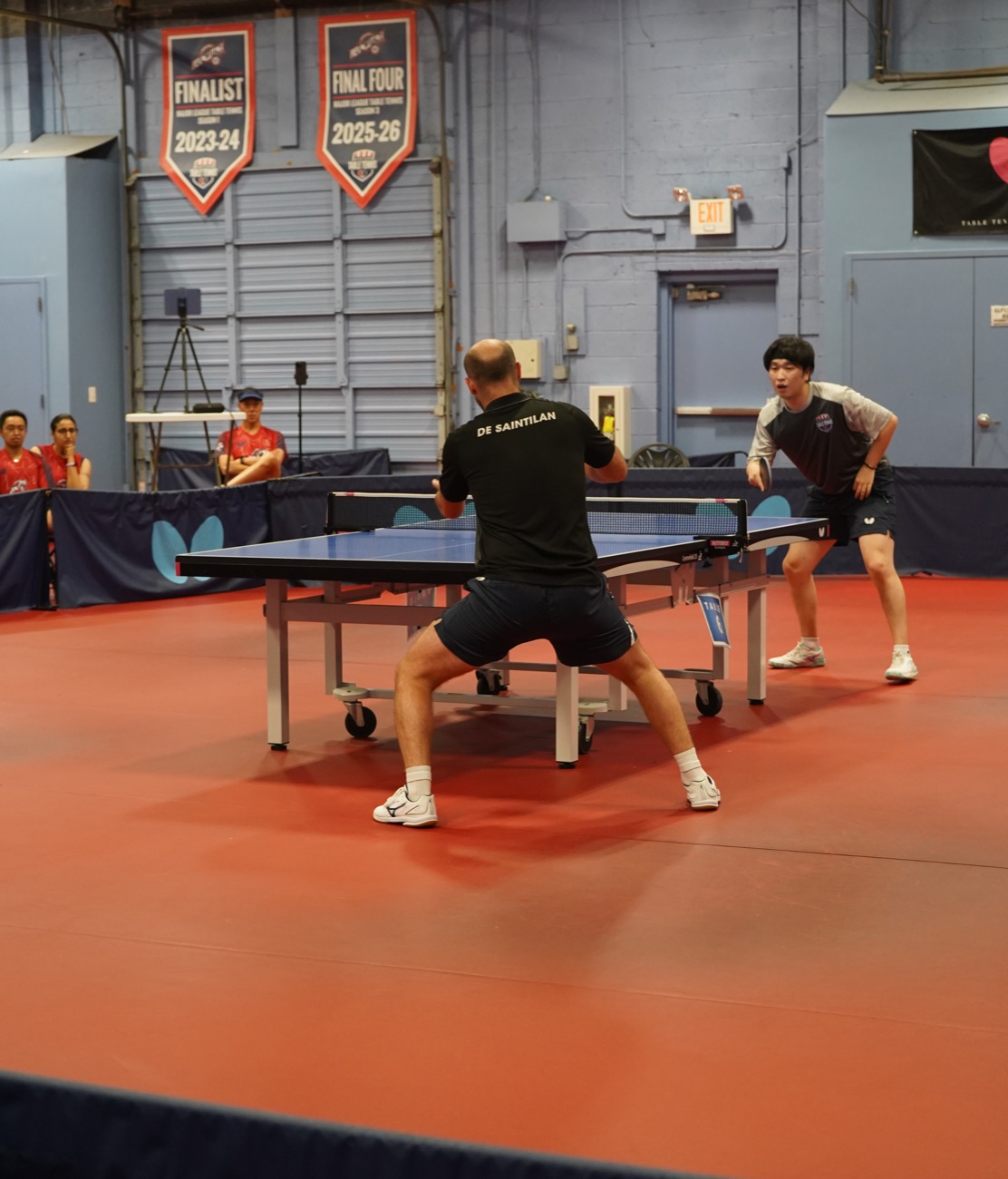 A player in a ready stance facing his opponent across the blue table
