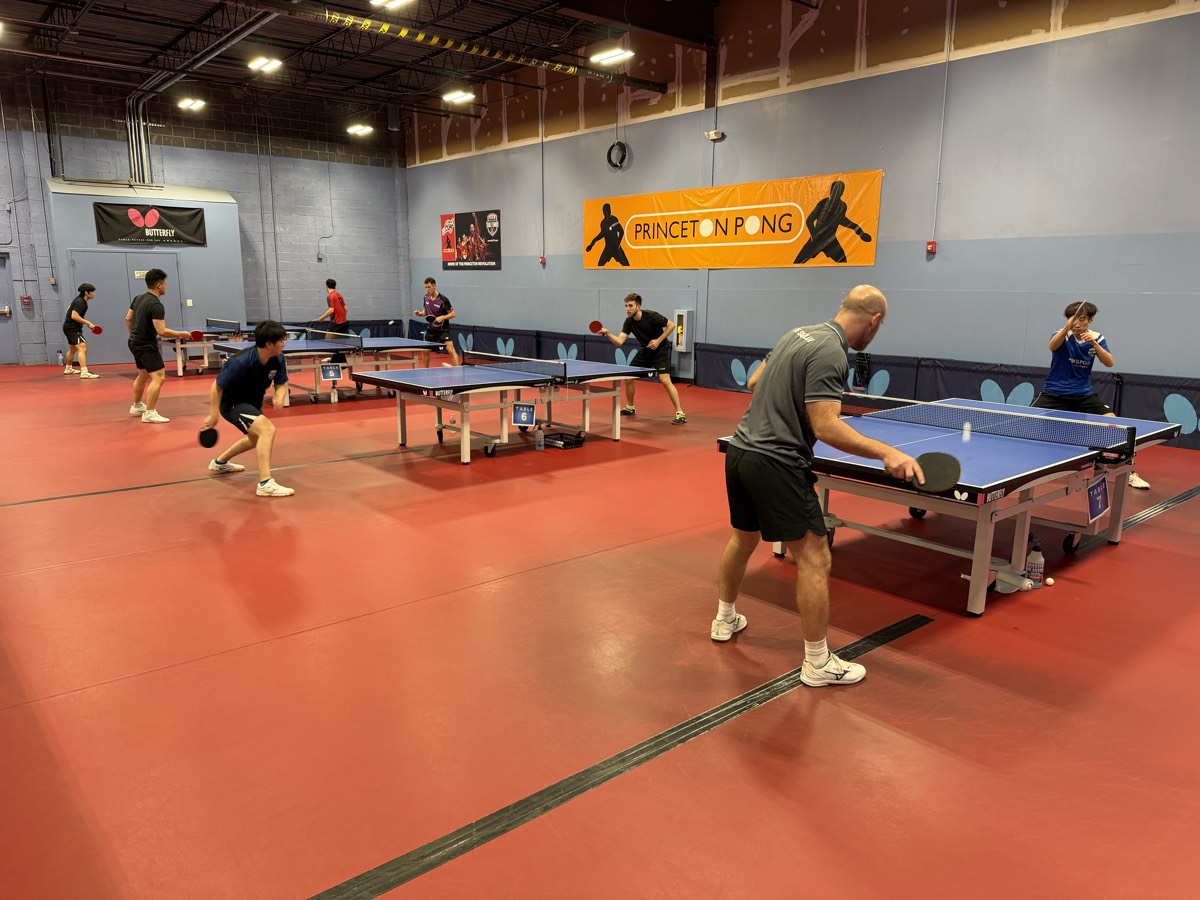 Wide view of the Princeton Pong floor with several matches in play across multiple tables during a tournament